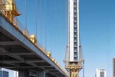 Imagen de una grúa grande en un sitio de construcción bajo un cielo azul, con la silueta de un edificio en progreso.